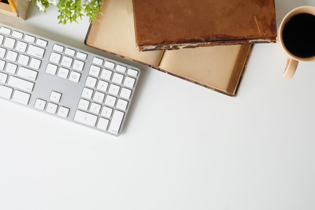 Top view office desk with computer keyboard, coffee, pencil, plant and books on white table.の写真素材