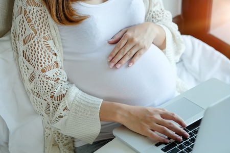 Pregnant woman is using laptop computer with learning a knowledge on bed.の写真素材
