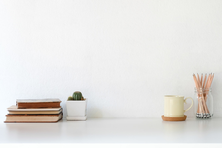 Workspace coffee mug, books, pencil and cactus on white desk.の写真素材