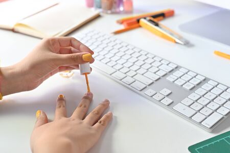 Cropped shot woman painting nails on office desk.