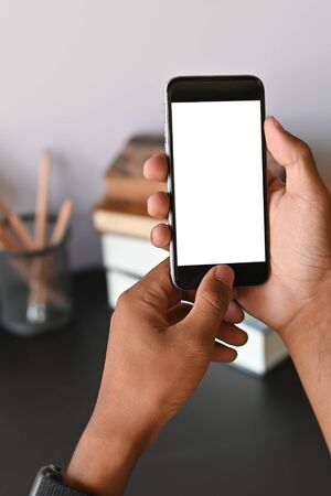Cropped shot of smartphone on hands with empty screen on office desk.の写真素材