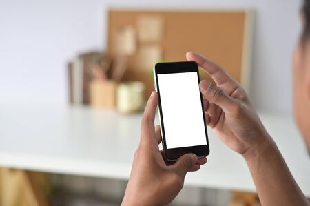 Man hands holding smart phone with blank copy space screen for your text message or information content, male reading text message on telephone during in office desk urban setting.の写真素材