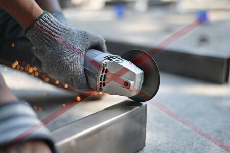 Uncomfortable Industrial Worker with Electric grinder cutting metal close up shot.
