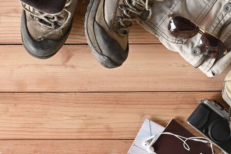 Travel accessories set on wooden desk hiking boots, jacket, backpack, map, camera and sunglasses with copy space.の写真素材
