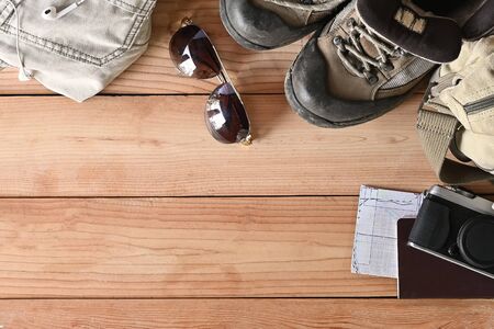 Travel accessories set on wooden desk hiking boots, jacket, backpack, map, camera and sunglasses with copy space.の写真素材