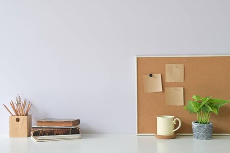 Workspace with books, coffee, pencil, plant and sticky note paper on board with office white desk.の写真素材