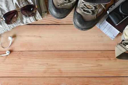 Travel accessories set on wooden desk hiking boots, jacket, backpack, map, camera and sunglasses...