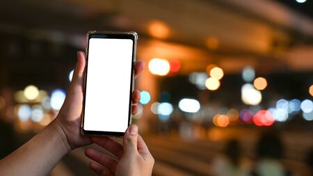 Mockup smartphone on hands with empty screen and bokeh on blur night city background.の写真素材