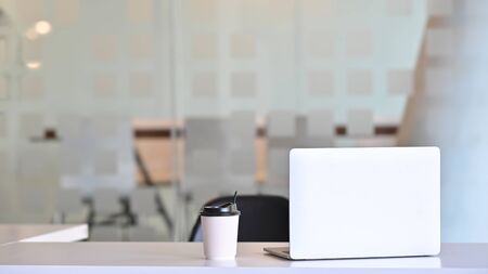 Workspace laptop computer and coffee paper cup on table front of meeting room.の写真素材