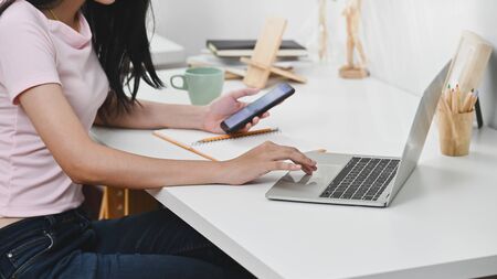Cropped shot young woman using laptop and smartphone on workplace.の写真素材