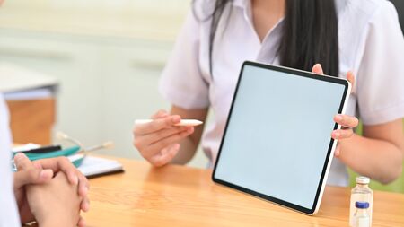 Cropped shot of female doctor explain symptoms to patient with digital tablet on table.の写真素材