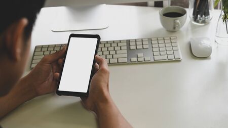 Man's hand holding smartphone with blank screen in his office. Blank screen mobile phone for graphic display montage.の写真素材