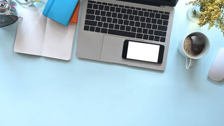 Office desk laptop, mockup smartphone with coffee on blue background.