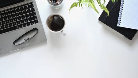 Creative flat lay office desk. Top view table with laptop, notebooks and coffee cup on white...