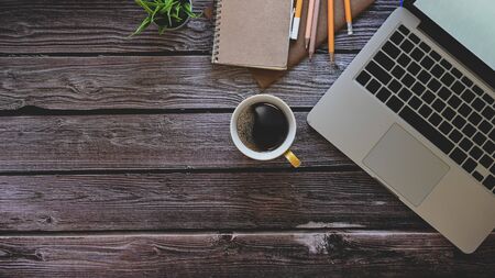 Laptop computer, notebook, pencil with coffee and plant on wooden table.の写真素材
