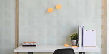 Workspace office desk with notebook, calender, sticky note and document file on white table with glass windows.の写真素材