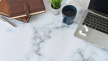 Modern office desk with laptop, coffee, earphones, notebook and pencil on marble table.