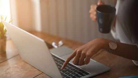 Closeup female using laptop and holding coffee cup.の写真素材