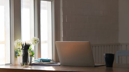 Front view home workspace with laptop, coffee, pencil holder and flower on wooden table.の写真素材