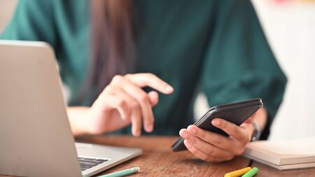 Cropped shot woman using her mobile phone on table.の写真素材