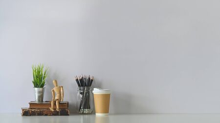 Decorative workspace with books, dummy model, coffee, pencil and house plant on white table.の写真素材