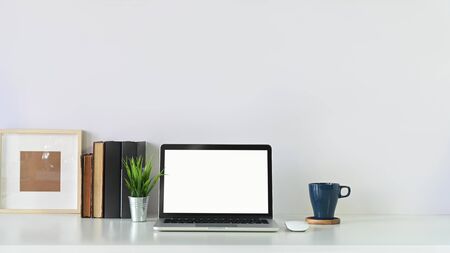 Workspace laptop computer, book, photo frame and coffee mug with plant pot on copy space white table.の写真素材