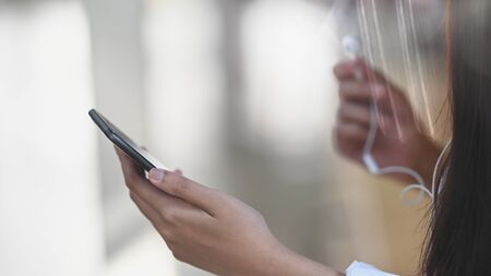 Streaming music concept, Closeup female holding mobile phone and earphones.