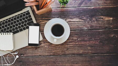 Top view wood table with mockup mobile phone, laptop, coffee, earphone, notepad and pencil.