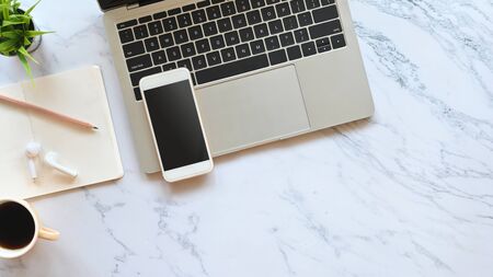 Laptop, black blank screen smartphone, wireless earphone, pencil, notes and potted plant putting on the marble table. Flat lay working equipment concept.の写真素材