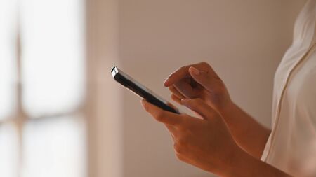 Side shot of beautiful businesswoman in white shirt surfing the internet by using smartphone in her...
