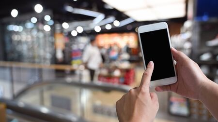 Close-up image of male hands using black blank screen smartphone at shopping center. Searching or social networks concept, Blurred background .の写真素材