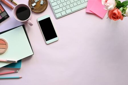 Top view image of woman accessories putting on the pink working desk, including keyboard, coffee cup, bouquet, notebook, pen, mobile, cosmetics and paper clip. Feminine working desk concept.の写真素材
