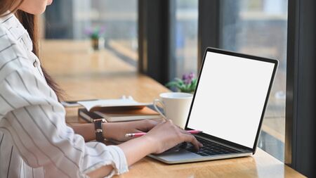 Close-up image of beautiful business woman sitting at the wooden work desk and typing on the white...