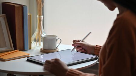 Cropped shot side view of young creative woman drawing/using on a white blank screen computer tablet...