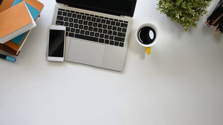 Modern office working desk including a coffee cup, laptop, black blank screen smartphone, potted plant, pencil and books putting on it. Office equipment with flat laid.の写真素材