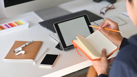 Back view Cropped shot of young creative man while taking note and concentrating on his blank screen tablet at the work desk. の写真素材