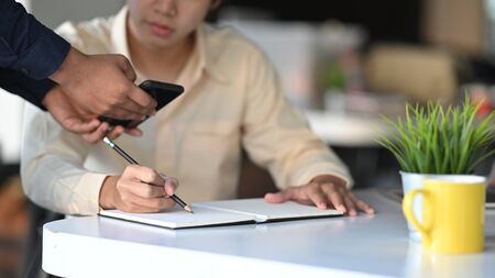 Cropped shot of young architect writing/drawing roughly the house architectural concept by copying from the customer smartphone.の写真素材
