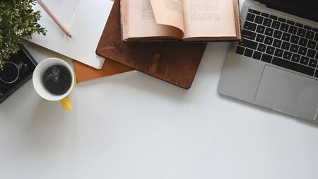 Modern office desk include laptop, camera, coffee cup, notebook, book, potted plant and pencil. Top view of office desk and office equipment.の写真素材