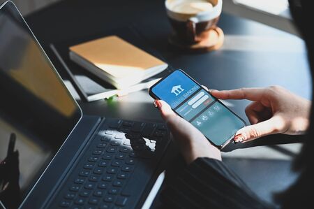 Cropped shot of executive woman holding smartphone in hands while doing online financial transaction by her smartphone in front computer tablet at the modern working desk.の写真素材