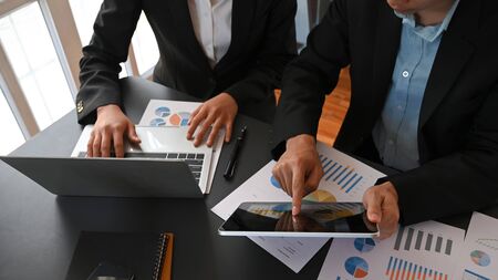 Cropped image of business people talking/meeting/discussing about their business plan by using a computer laptop and tablet with graphic charts at the meeting table with office as background.の写真素材