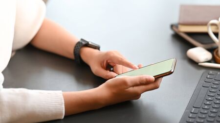 Cropped image of creative woman working as graphic designer holding on smartphone while sitting at the modern working table with comfortable living room as background.の写真素材