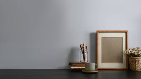 Workspace pencil holder, Stack of books, Picture frame, Coffee cup and potted flower putting together on comfortable working table with living room as background. Orderly working space concept.の写真素材