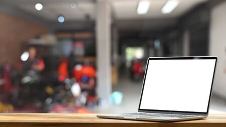 Computer laptop with empty white screen putting on modern wooden table in blurred garage as background.の写真素材