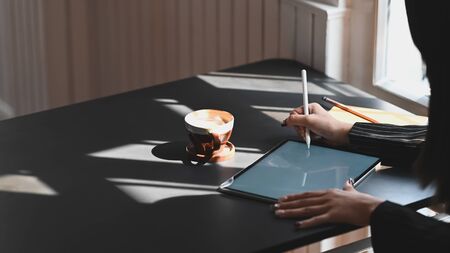 Cropped shot of young executive woman drawing on the computer tablet with white blank screen while...