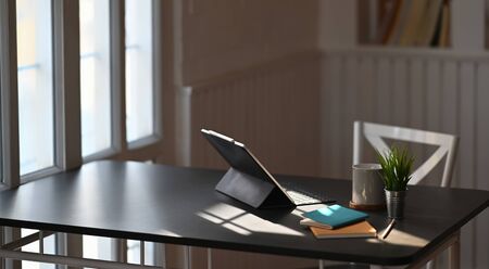 Photo of sunlight shining through the window to black working desk. Computer tablet, notebook,...