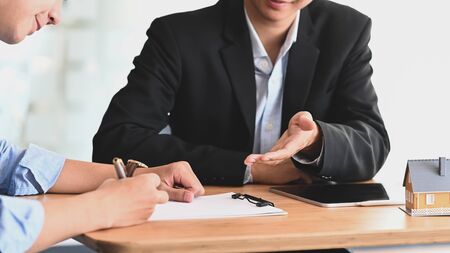 Cropped shot of Real estate agent offer house insurance or house ownership to smart man in blue shirt at the modern wooden table. Signing on agreement, Broker/Seller/Dealer concept.の写真素材