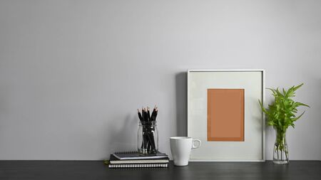 Photo of notes, diary, picture frame, potted plant, coffee cup and pencil holder putting together on modern working table with white wall as background. Orderly workplace concept.の写真素材