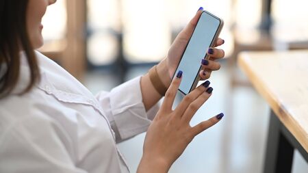 Photo of beautiful woman holding a smartphone in her hands while sitting and lean on chair at the...