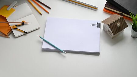 Photo of Architect working table with accessories putting on it. Flat lay Model house, Ruler, Notebook, Pencils, Drawing compasses, Potted plant and document file. Orderly/Comfortable workplace.の写真素材