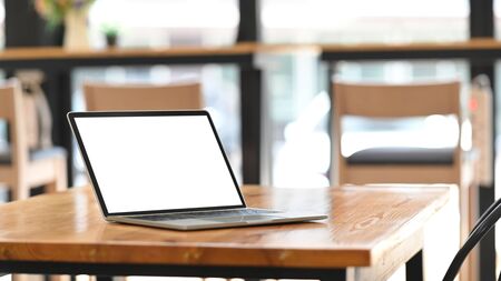Photo of white blank screen computer laptop putting on wooden working desk over modern cafe/restaurant as background. Orderly workplace concept. Space for advertisement.の写真素材